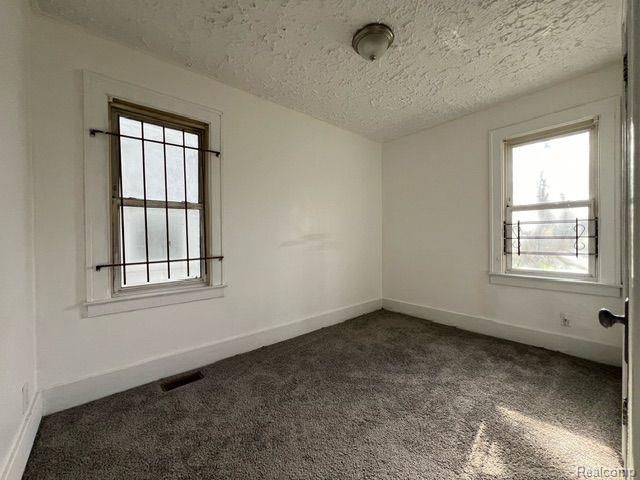 spare room featuring visible vents, dark colored carpet, baseboards, and a textured ceiling