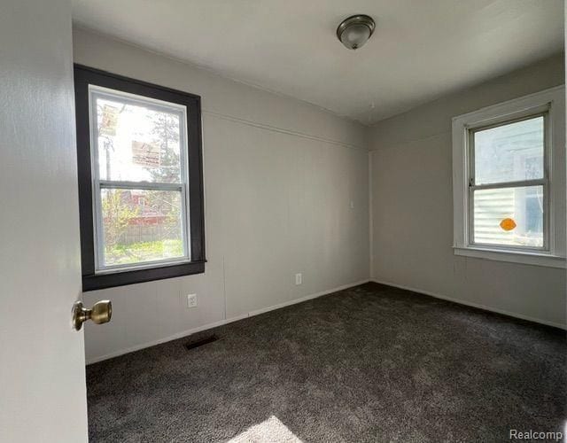 empty room with dark carpet, baseboards, and visible vents