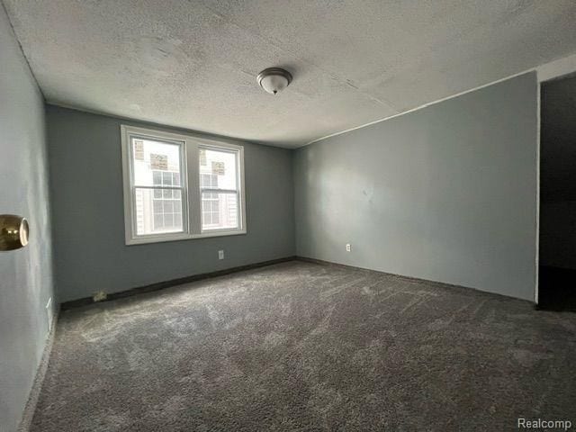 unfurnished room with dark carpet and a textured ceiling