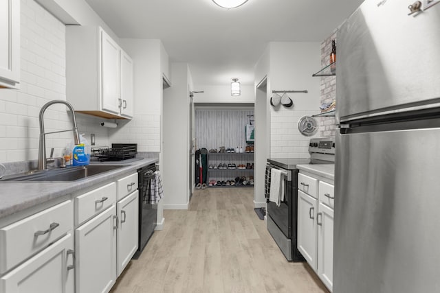 kitchen with light wood-style flooring, a sink, tasteful backsplash, white cabinetry, and appliances with stainless steel finishes