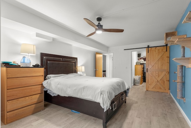 bedroom with light wood-style flooring, ceiling fan, and a barn door