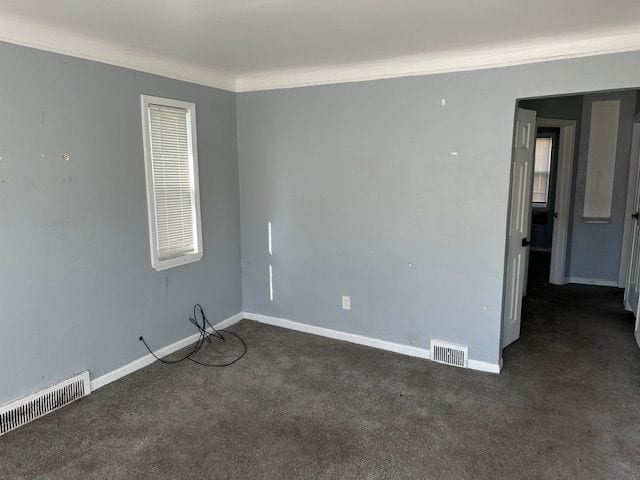 unfurnished room with dark carpet, visible vents, and crown molding