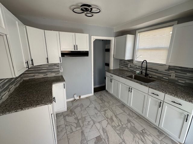 kitchen with marble finish floor, dark stone countertops, a sink, tasteful backsplash, and white cabinetry