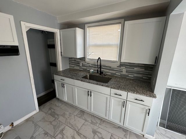 kitchen featuring decorative backsplash, marble finish floor, a sink, and dark stone countertops