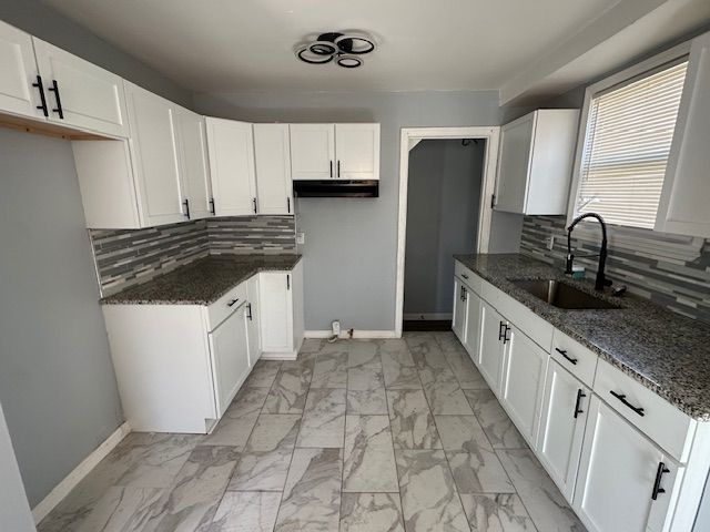kitchen with marble finish floor, dark stone countertops, backsplash, a sink, and baseboards