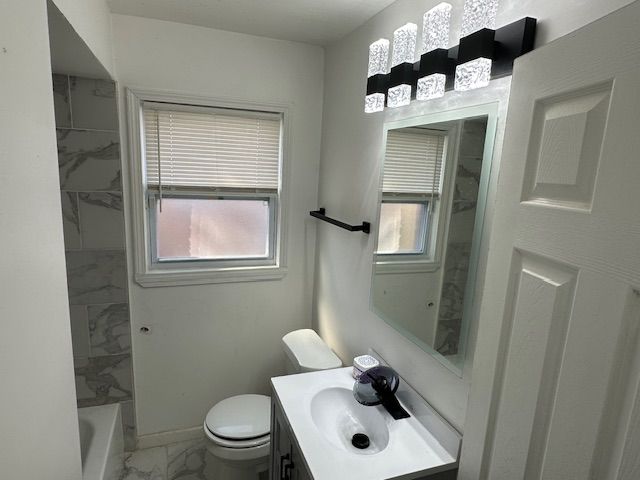 bathroom featuring a healthy amount of sunlight, marble finish floor, vanity, and toilet