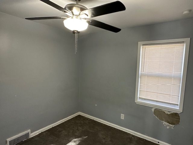 empty room featuring baseboards, a ceiling fan, visible vents, and dark carpet