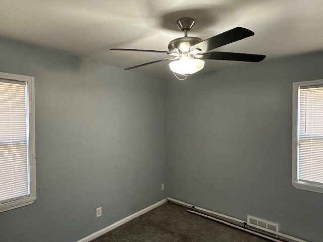 spare room with dark carpet, visible vents, a ceiling fan, and baseboards