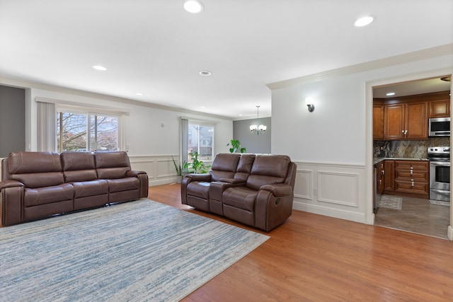 living room featuring wainscoting, an inviting chandelier, a decorative wall, and crown molding