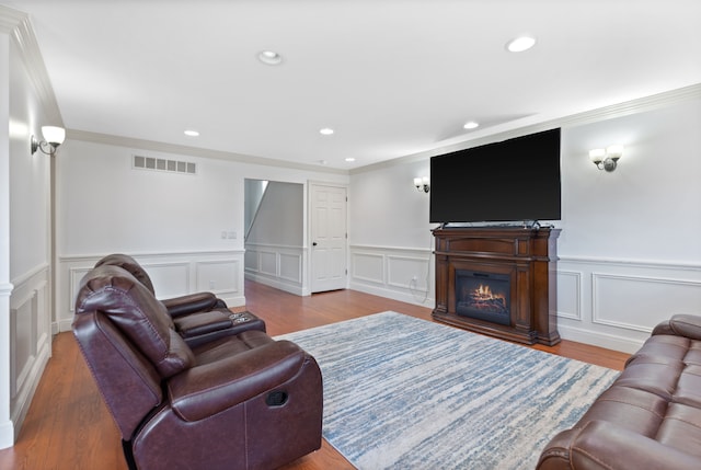 living area featuring a wainscoted wall, a glass covered fireplace, visible vents, a decorative wall, and ornamental molding