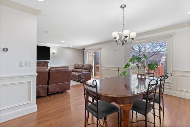 dining room with ornamental molding, a decorative wall, wainscoting, a chandelier, and light wood-style flooring