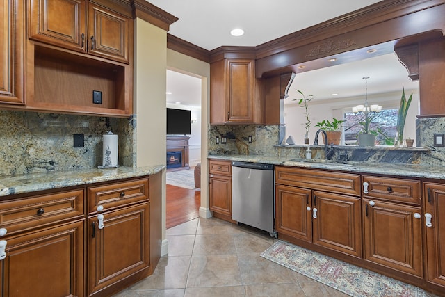 kitchen featuring a warm lit fireplace, dishwasher, a sink, decorative backsplash, and a notable chandelier