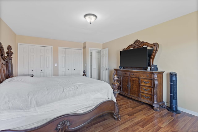 bedroom with baseboards, wood finished floors, and two closets