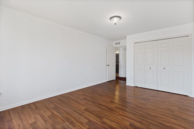 unfurnished bedroom featuring visible vents, baseboards, a closet, and dark wood-style flooring