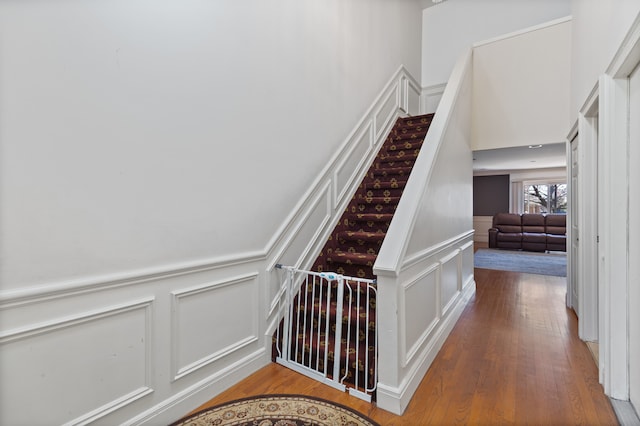 stairway with a decorative wall, a wainscoted wall, and wood finished floors