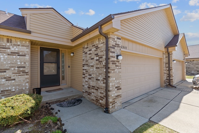 entrance to property featuring a garage, brick siding, concrete driveway, and roof with shingles