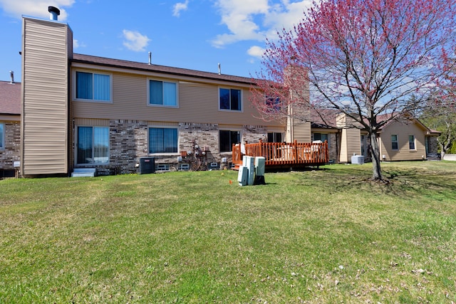 rear view of house featuring a chimney, central air condition unit, a lawn, a deck, and brick siding