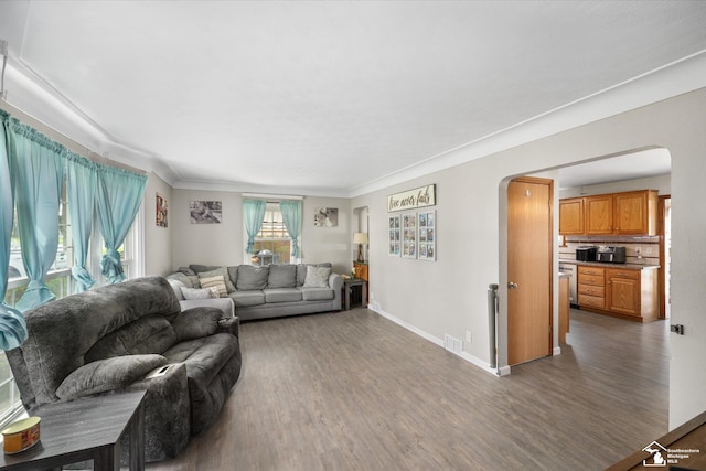 living area featuring arched walkways, visible vents, baseboards, wood finished floors, and ornamental molding