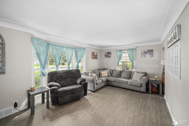 living area with baseboards, wood finished floors, visible vents, and ornamental molding