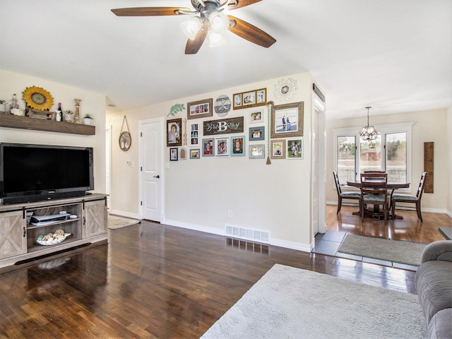 living room featuring baseboards, dark wood-type flooring, visible vents, and ceiling fan with notable chandelier