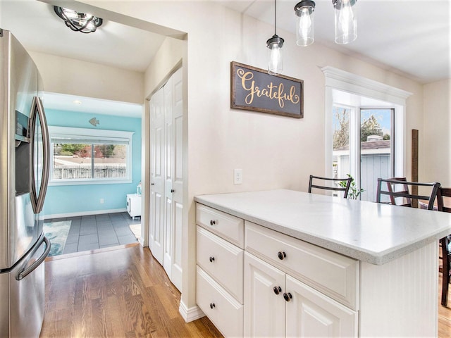 kitchen featuring light countertops, wood finished floors, stainless steel fridge, and white cabinetry