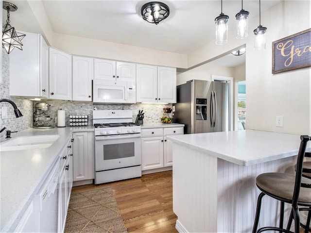 kitchen with a peninsula, a kitchen breakfast bar, a sink, decorative backsplash, and white appliances