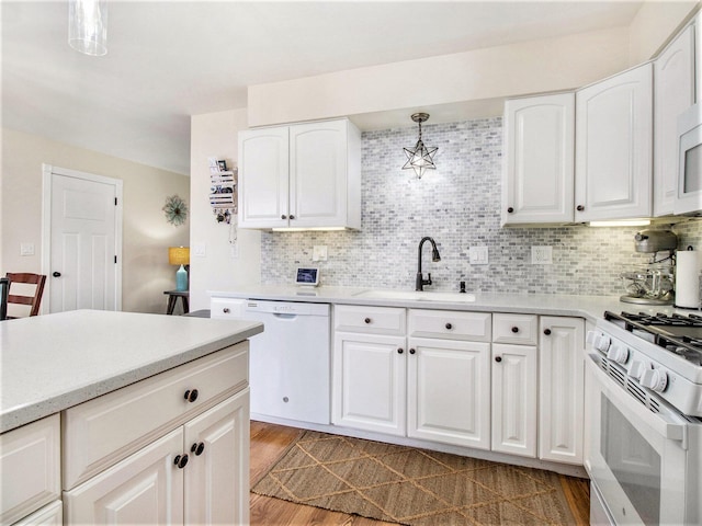 kitchen featuring decorative backsplash, light countertops, white appliances, and a sink