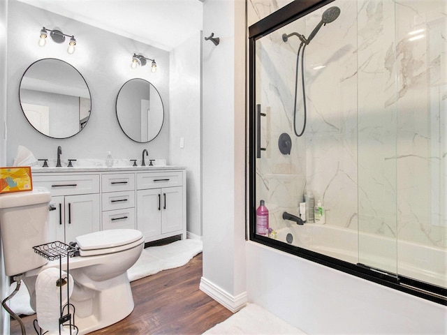 bathroom with toilet, wood finished floors, a sink, and combined bath / shower with glass door