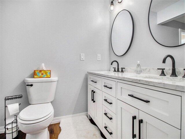 bathroom featuring toilet, a sink, double vanity, and baseboards