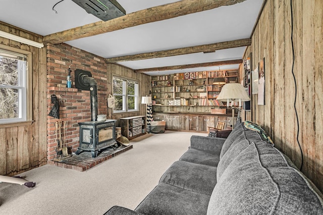 living room featuring beam ceiling, wooden walls, carpet, and a wood stove