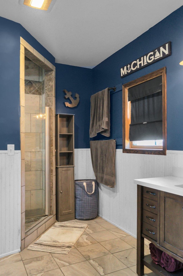 full bath with vanity, a wainscoted wall, and a stall shower