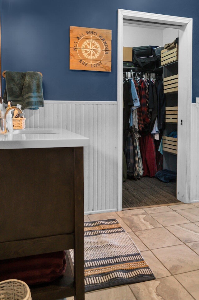bedroom with light tile patterned flooring, a closet, a wainscoted wall, and a sink
