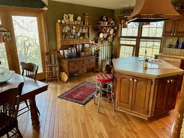 kitchen featuring light wood finished floors, custom exhaust hood, wallpapered walls, light countertops, and cooktop