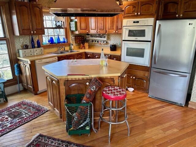 kitchen featuring light wood finished floors, light countertops, white appliances, and a sink