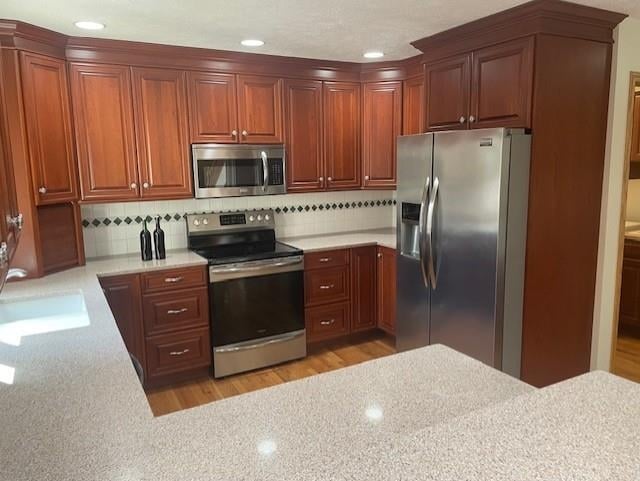 kitchen featuring light stone counters, tasteful backsplash, a sink, stainless steel appliances, and light wood finished floors