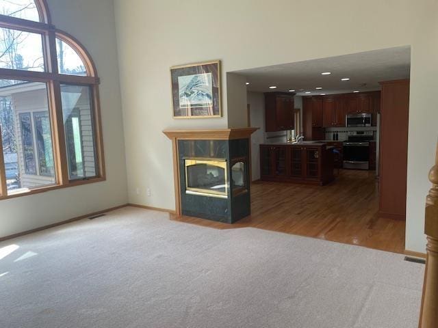 unfurnished living room with recessed lighting, a high ceiling, light carpet, baseboards, and a fireplace