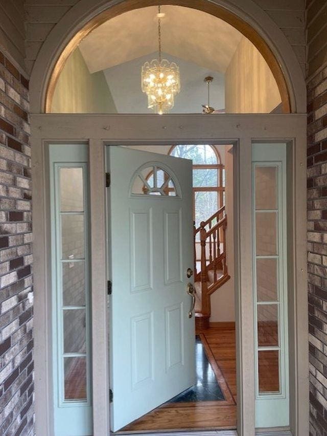 entrance foyer featuring brick wall, arched walkways, lofted ceiling, and a chandelier