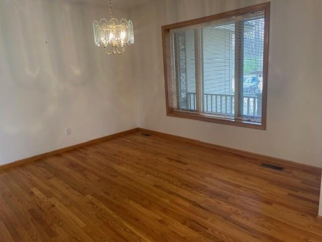 unfurnished room featuring visible vents, baseboards, wood finished floors, and a chandelier