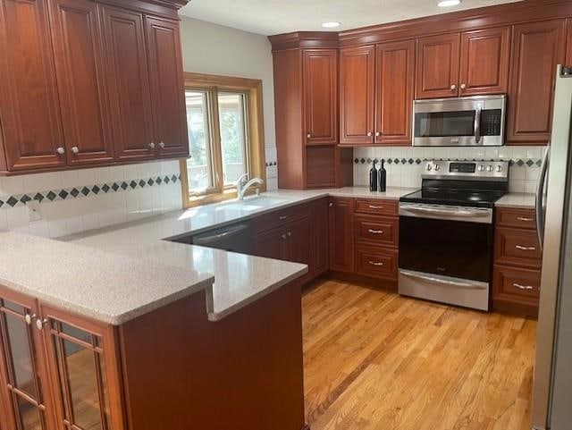 kitchen with a sink, light wood finished floors, backsplash, a peninsula, and appliances with stainless steel finishes
