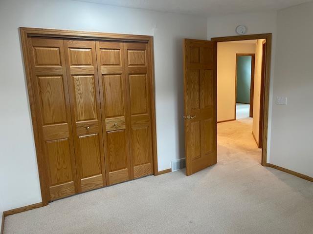 unfurnished bedroom with light carpet, baseboards, and a closet