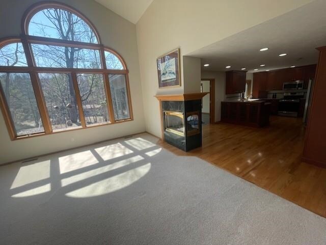 unfurnished living room with high vaulted ceiling, carpet flooring, wood finished floors, and a fireplace