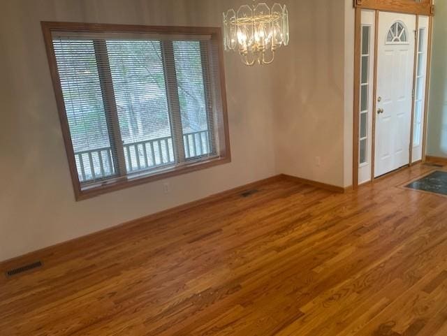 unfurnished dining area with wood finished floors, visible vents, baseboards, and an inviting chandelier