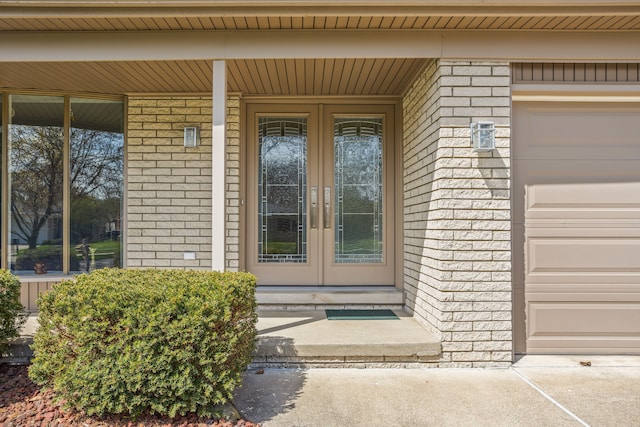 view of exterior entry featuring brick siding, a garage, french doors, and a porch