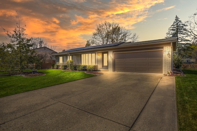 view of front of home featuring a garage, brick siding, concrete driveway, a lawn, and solar panels