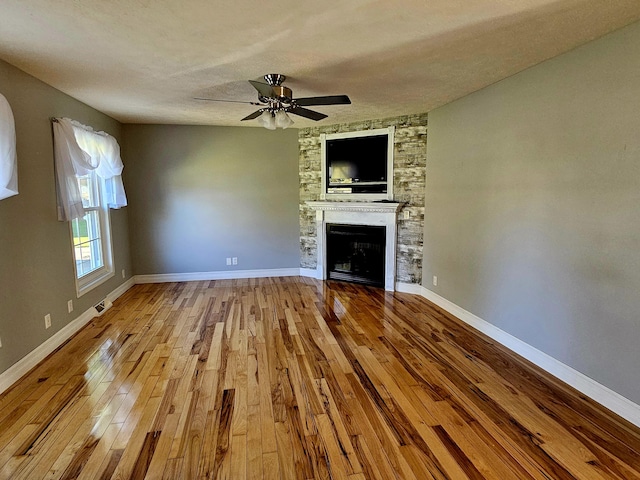 unfurnished living room featuring a ceiling fan, hardwood / wood-style floors, a textured ceiling, a fireplace, and baseboards