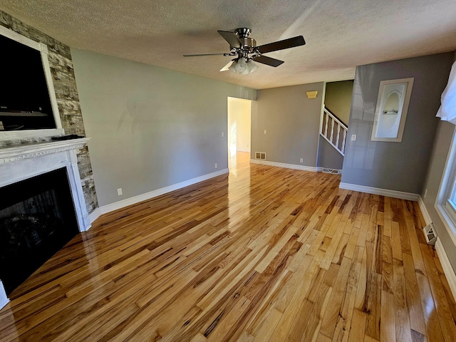 unfurnished living room with stairway, a ceiling fan, wood finished floors, a textured ceiling, and visible vents