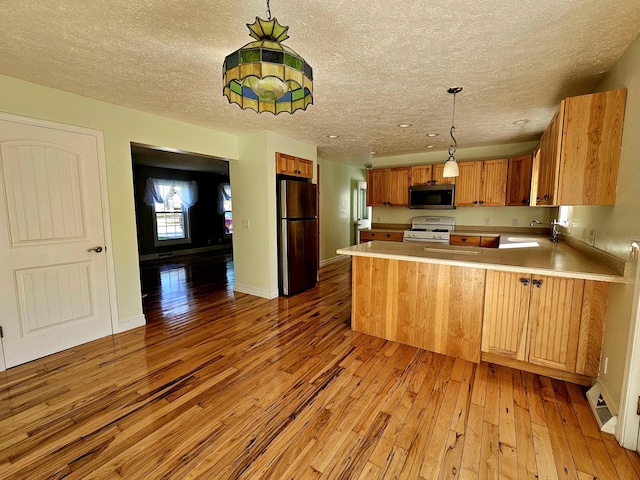 kitchen with white gas range, light wood-style flooring, stainless steel microwave, a peninsula, and freestanding refrigerator