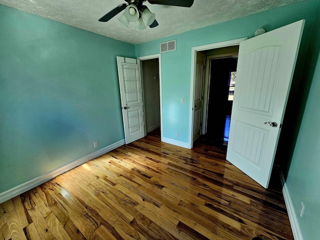 unfurnished bedroom featuring a textured ceiling, baseboards, visible vents, wood finished floors, and ceiling fan