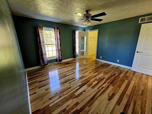 spare room featuring wood finished floors, a textured ceiling, ceiling fan, baseboards, and visible vents