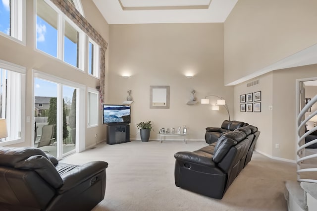 carpeted living room with visible vents, a high ceiling, baseboards, and stairs